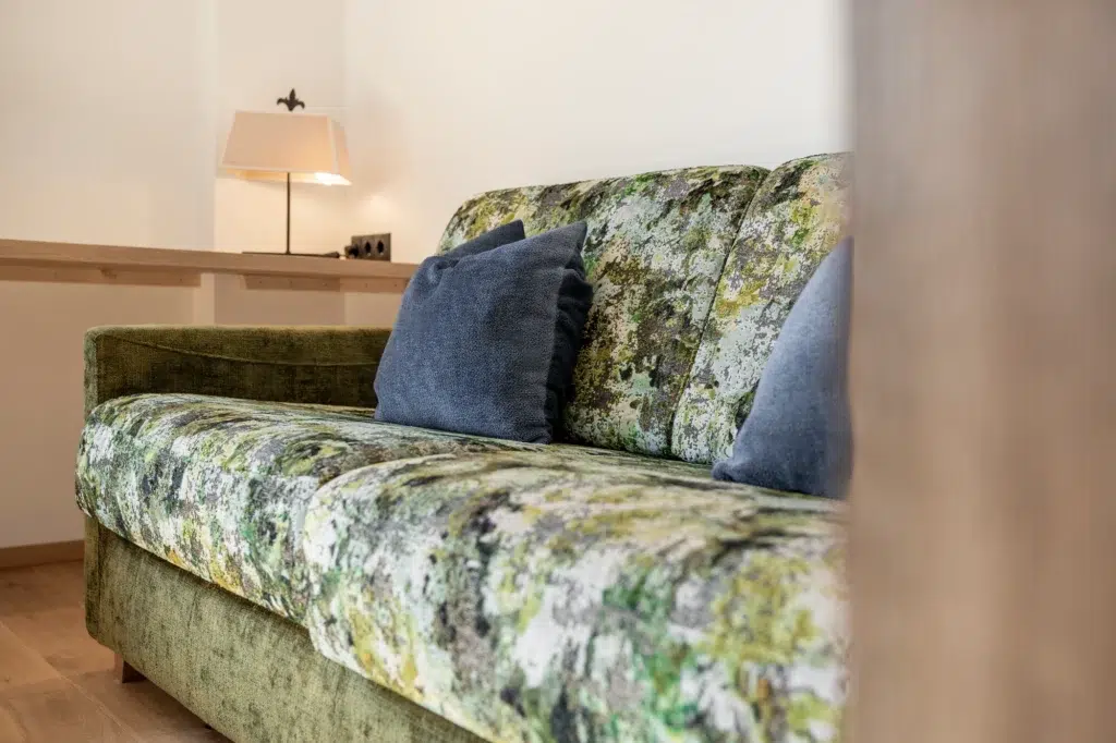 Grün gemustertes Sofa mit zwei blauen Kissen; perfekt für Ihren Rückzugsort ferienwohnung Seefeld.
