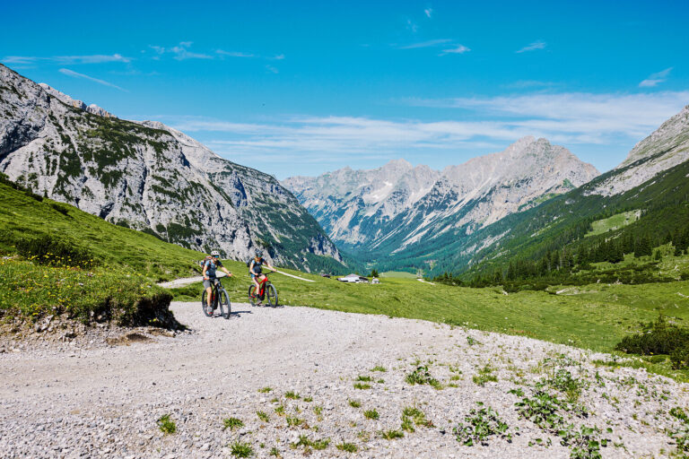 Zwei Radfahrer fahren in der Nähe des 4-Sterne-Hotels Seefeld, mit malerischen Gipfeln und grünen Tälern hinter ihnen.