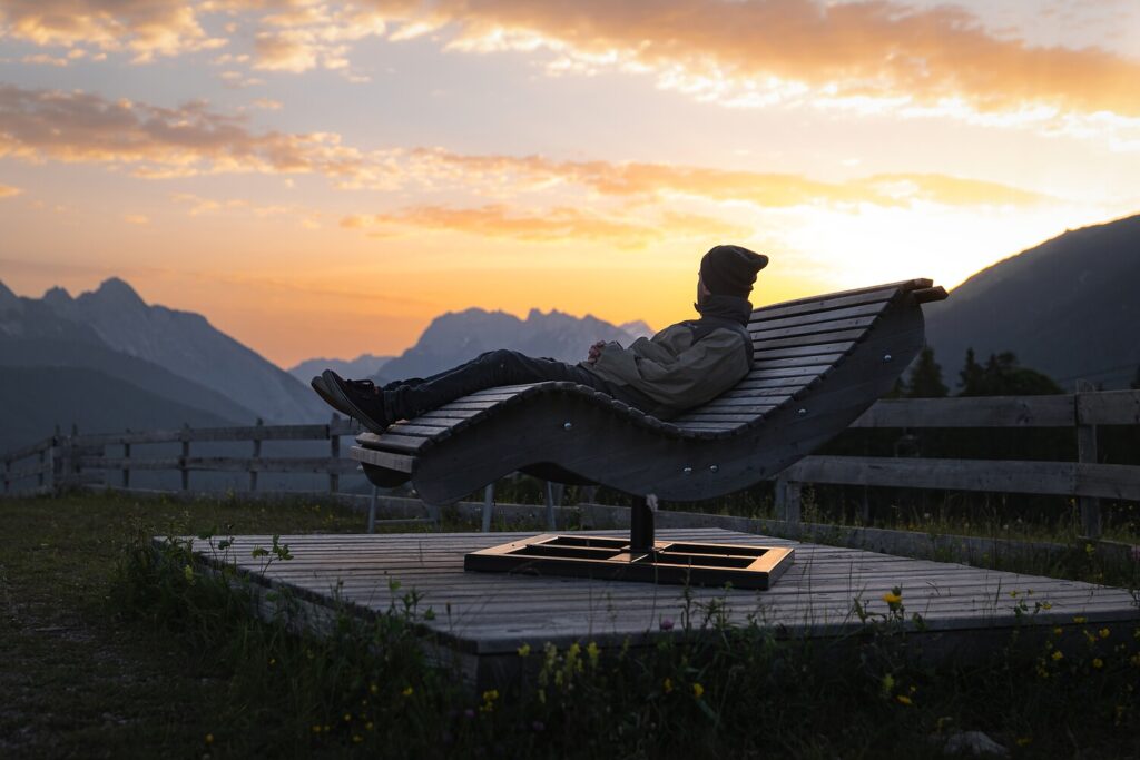 Person, die nach einer Wanderung in Seefeld auf einem hölzernen Liegestuhl entspannt und den Sonnenuntergang über den Bergen beobachtet.