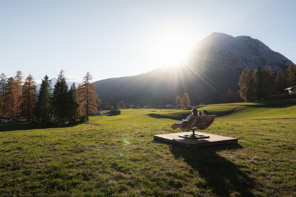 Person, die auf einer Bank auf einer sonnigen Seefelder Herbsturlaubswiese mit Bergblick entspannt.