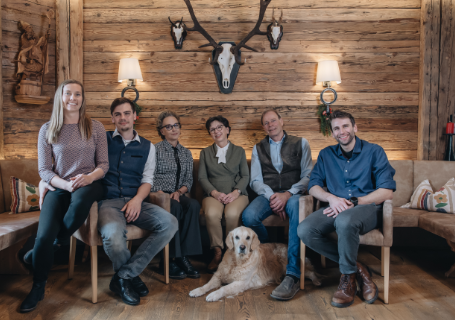 Sechs Erwachsene und ein Golden Retriever sitzen auf einem Sofa in einem rustikalen, holzgetäfelten Raum mit Geweih.