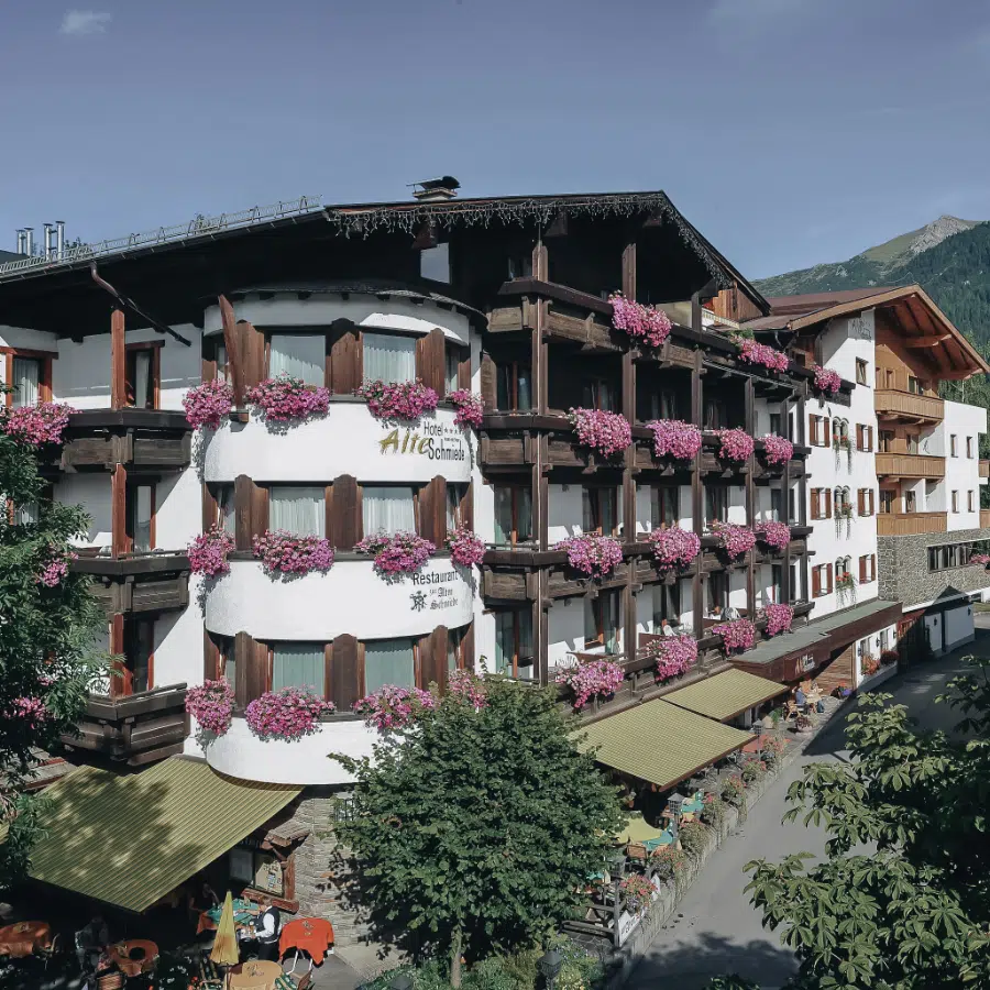 Charmantes 4-Sterne-Hotel in Seefeld mit Balkonen voller rosa Blumen vor der Bergkulisse.