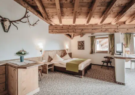 Gemütliches rustikales Schlafzimmer mit Holzbalken, Doppelbett, Schreibtisch und Hirschgeweih an der Wand.