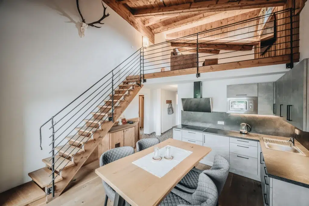 Moderne Loftküche in einer Ferienwohnung Seefeld mit Holztreppe und Gewölbedecke.