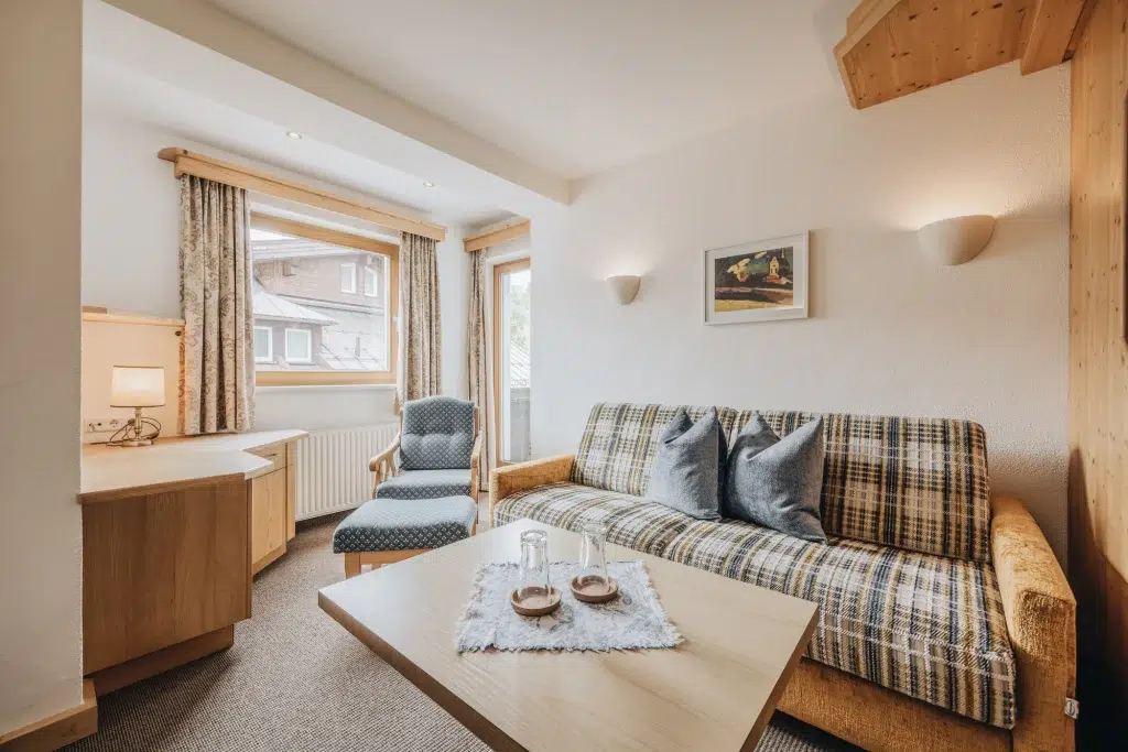 Gemütliches Wohnzimmer in einer Ferienwohnung Seefeld mit kariertem Sofa, Sessel, Schreibtisch und großem Fenster.