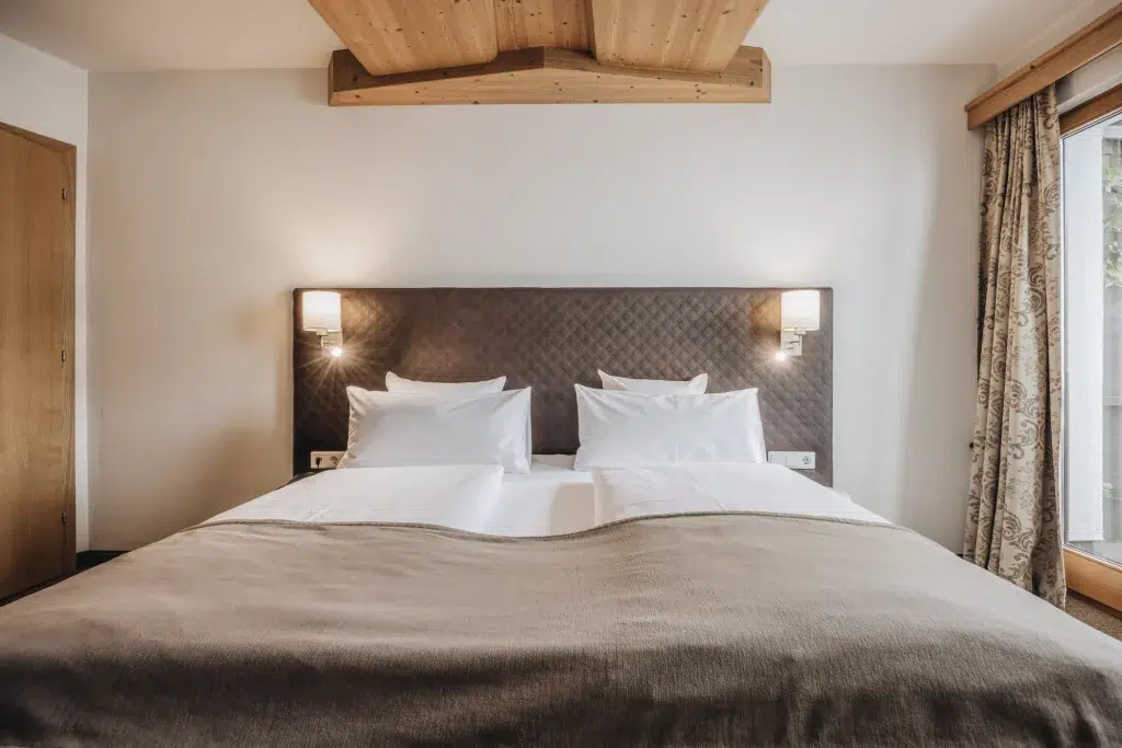 Ein ordentlich gemachtes Bett mit weißer Bettwäsche in einem gemütlichen Schlafzimmer mit Holzdecke in der Ferienwohnung Seefeld.