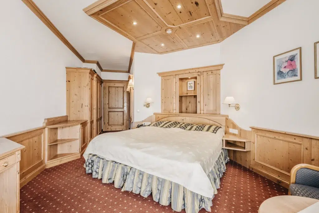 Gemütliches Seefeld-Doppelzimmer mit holzgetäfelten Möbeln, einem Doppelbett und gemustertem Teppich.