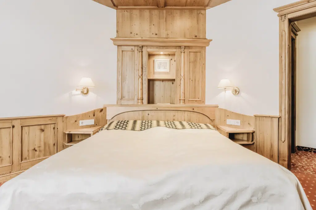 Gemütliches Seefeld Komfortzimmer mit Holzkopfteil, Wandlampen und einer leichten Decke auf dem Bett.