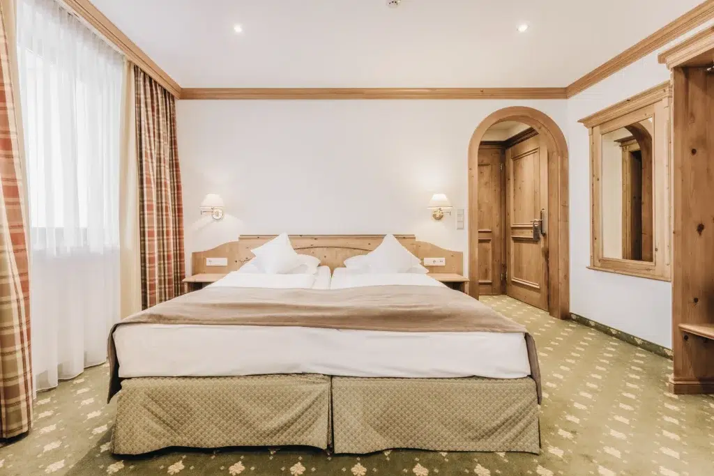 Seefeld Doppelzimmer mit Doppelbett, Holzakzenten, großem Fenster und grünem Teppich.