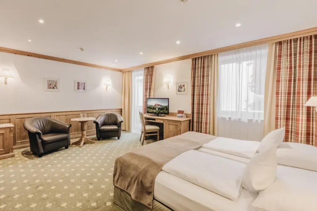 Helles Seefeld-Doppelzimmer mit Doppelbett, Schreibtisch, zwei Stühlen und großem Fenster mit karierten Vorhängen.