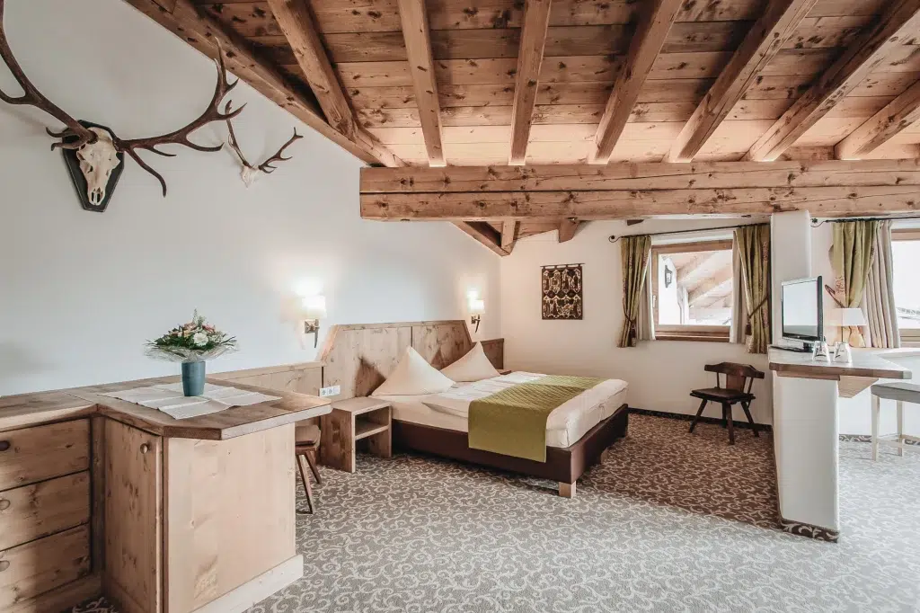 Gemütliches Seefeld Doppelzimmer mit Holzbalken, Geweih, Doppelbett und Tageslicht.