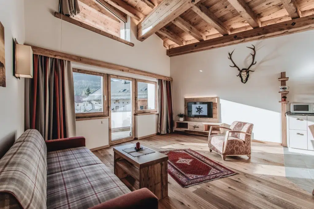 Gemütliches Wohnzimmer der Ferienwohnung Seefeld mit Holzdecke, kariertem Sofa, Fernseher und Hirschgeweih.