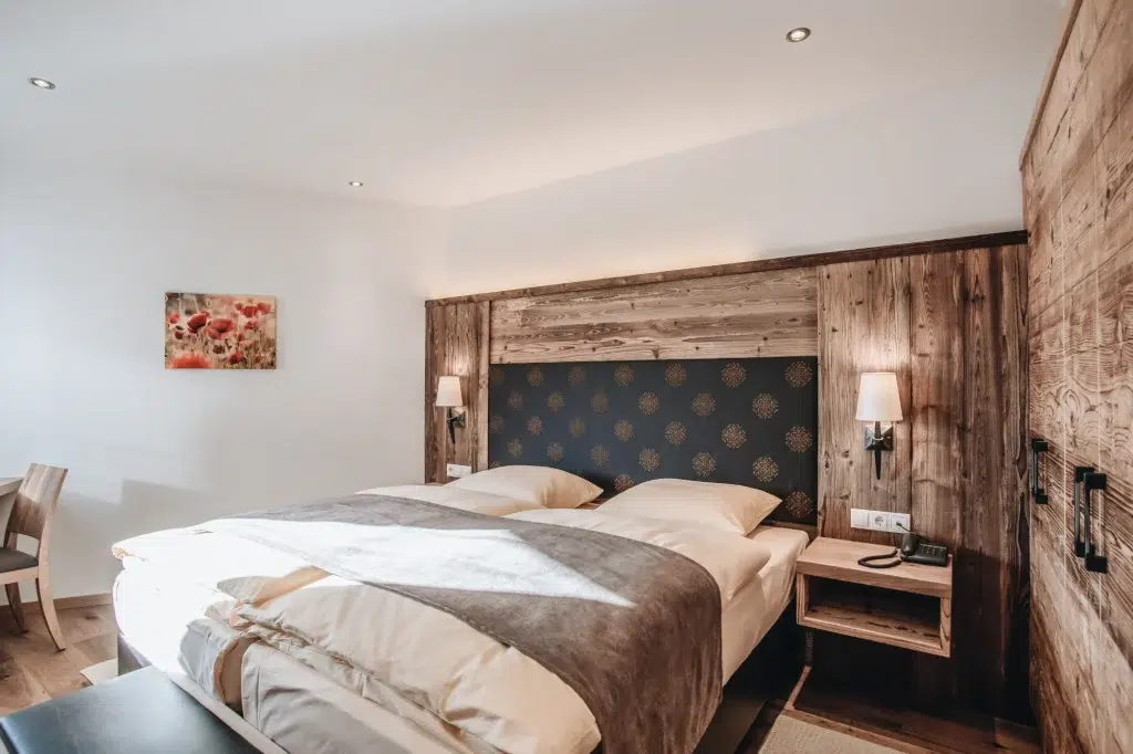 Gemütliches Zimmer in der Ferienwohnung Seefeld mit großem Bett, Holzakzenten und Blumengemälde.