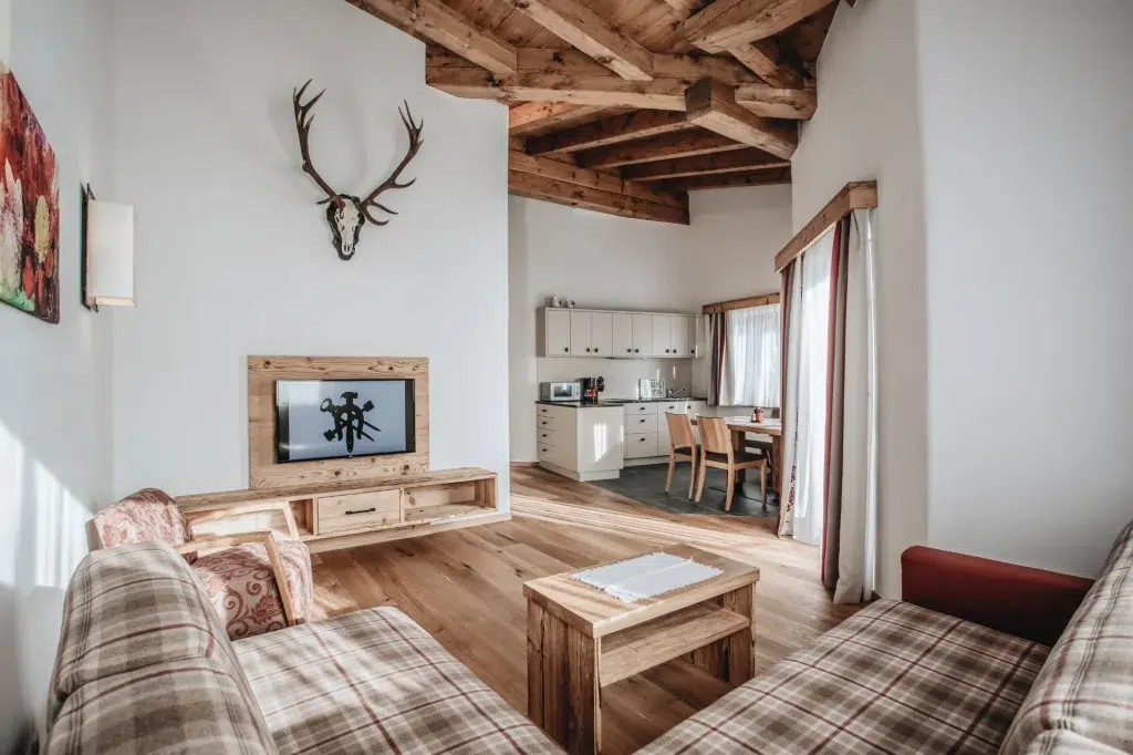 Gemütliches Wohnzimmer der Ferienwohnung Seefeld mit karierten Sofas, Holzmöbeln und einer Küche.