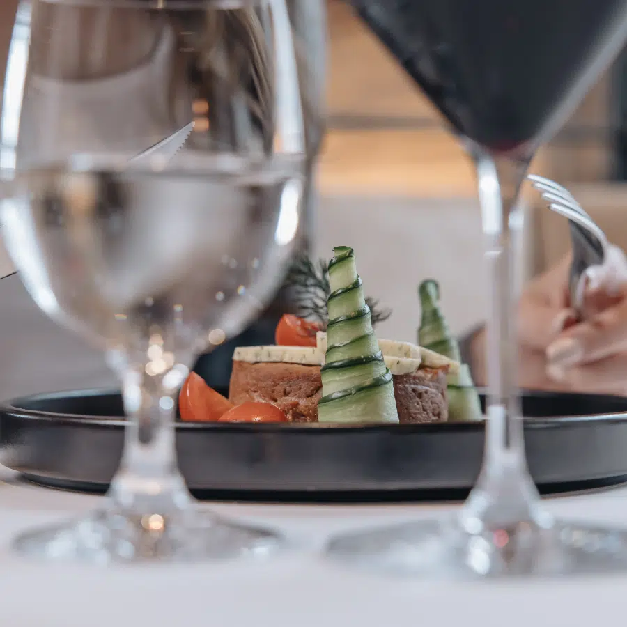 Elegantes Tellergericht mit Gemüse, gesehen durch Gläser mit Wasser und Rotwein auf einem Tisch.