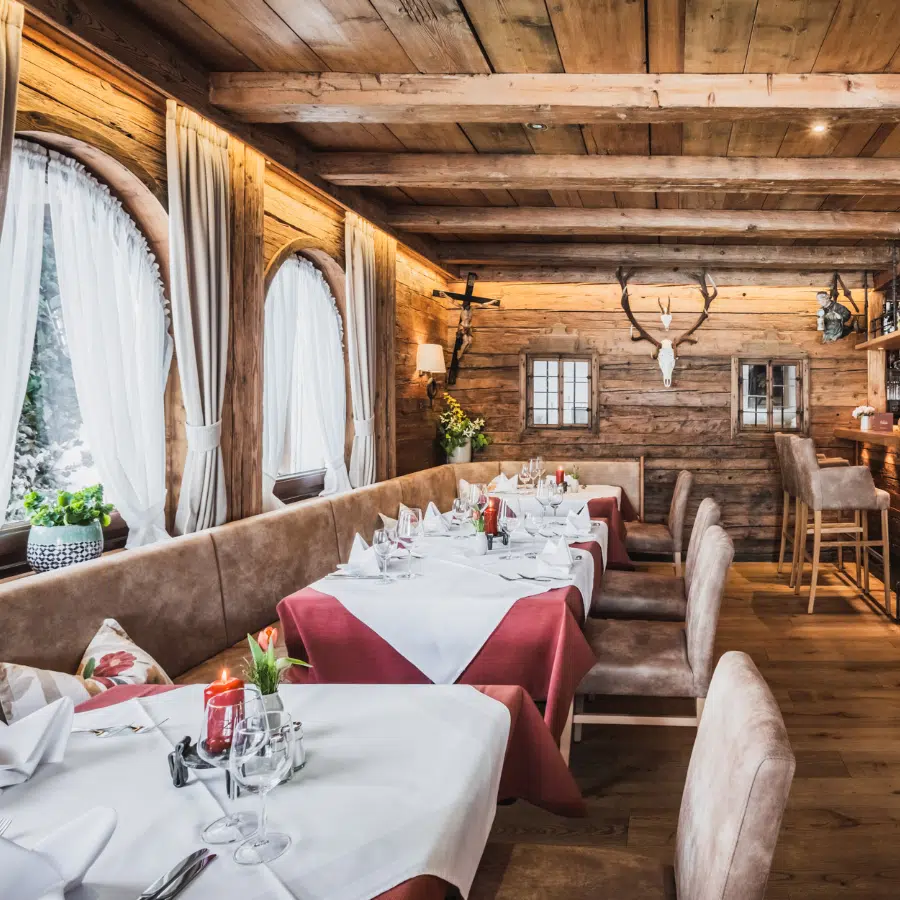 Rustikales Holzrestaurant im 4 Sterne Hotel Seefeld, mit gedeckten Tischen und Rundbogenfenstern.