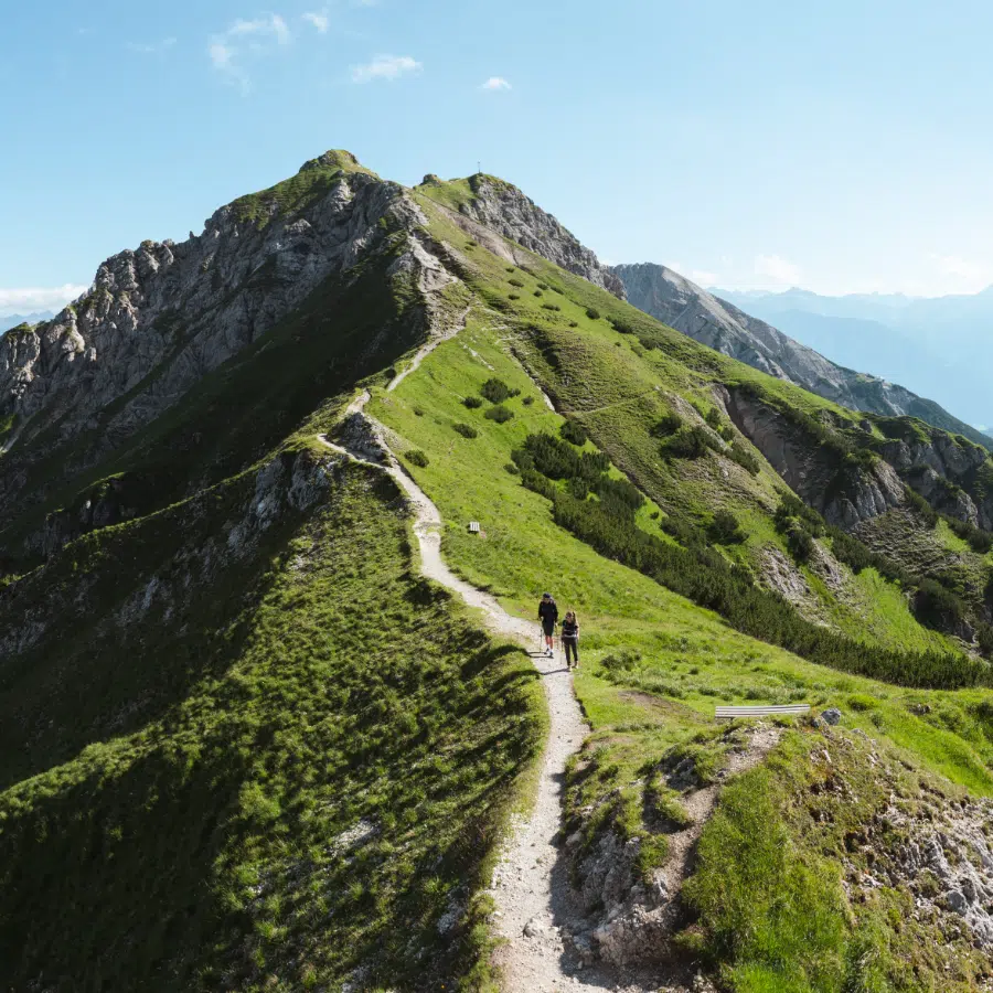 Zwei Wanderer genießen eine Wanderung auf einem schmalen Pfad auf einem grünen Bergrücken in Seefeld.
