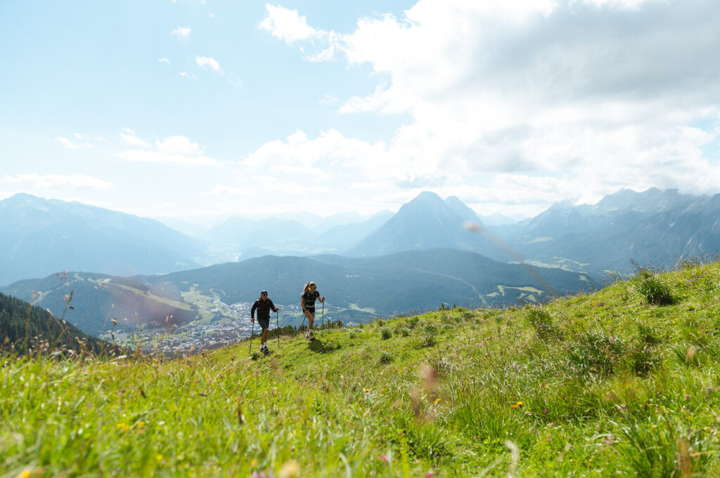Zwei Wanderer gehen einen grasbewachsenen Hügel hinauf, im Hintergrund ist der Seefelder Angebot Frühling im Bergtal zu sehen.