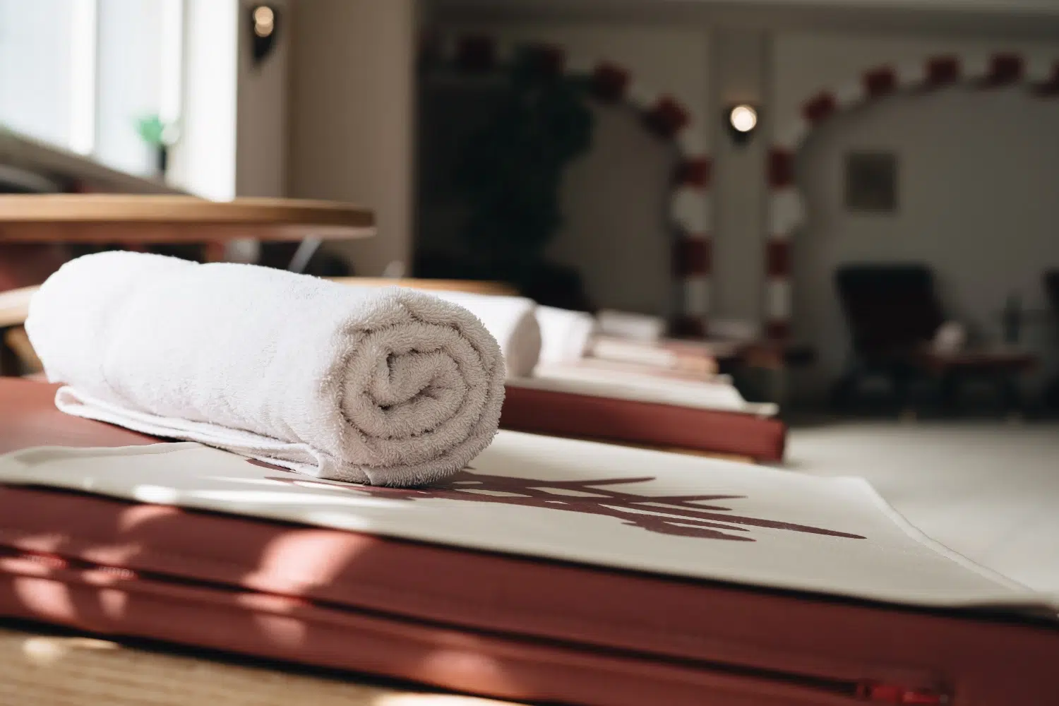 Ein aufgerolltes weißes Handtuch liegt auf einer gefalteten Matte im ruhigen Spa-Ambiente des Wellness Seefeld.