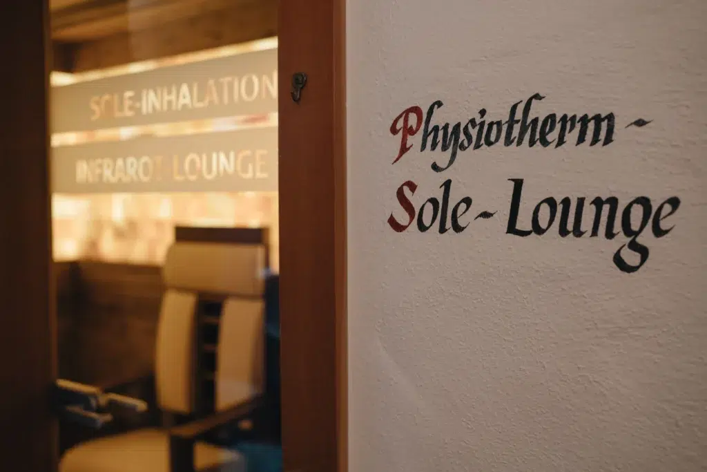 Wandschild mit der Aufschrift „Physiotherm Sole-Lounge“ im Wellness Seefeld, neben einem Raum mit Liegestuhl.
