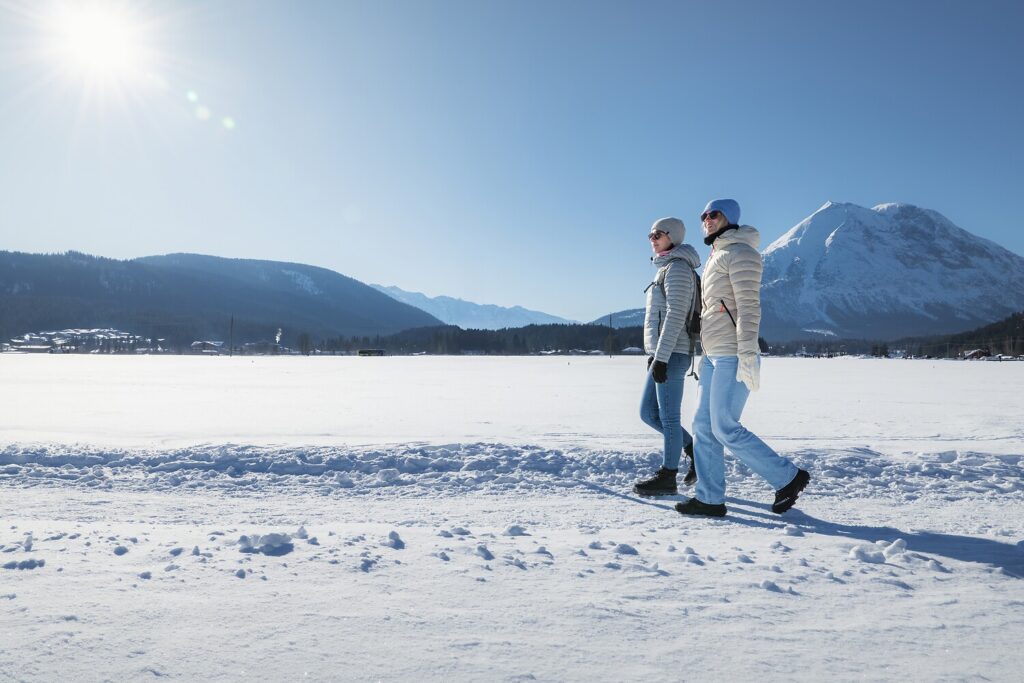 Zwei Menschen gehen auf verschneitem Boden in der Nähe des 4-Sterne-Hotels Seefeld, die Berge glänzen in der Sonne.