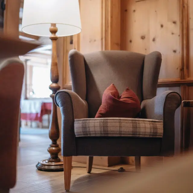 Grauer Sessel mit braunem Kissen neben einer Holzlampe in einem gemütlichen Zimmer mit Holzwänden.