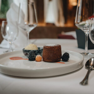 Schokoladenfondant mit Beeren und Eiscreme auf einem weißen Teller, gedeckt auf einem Restauranttisch.