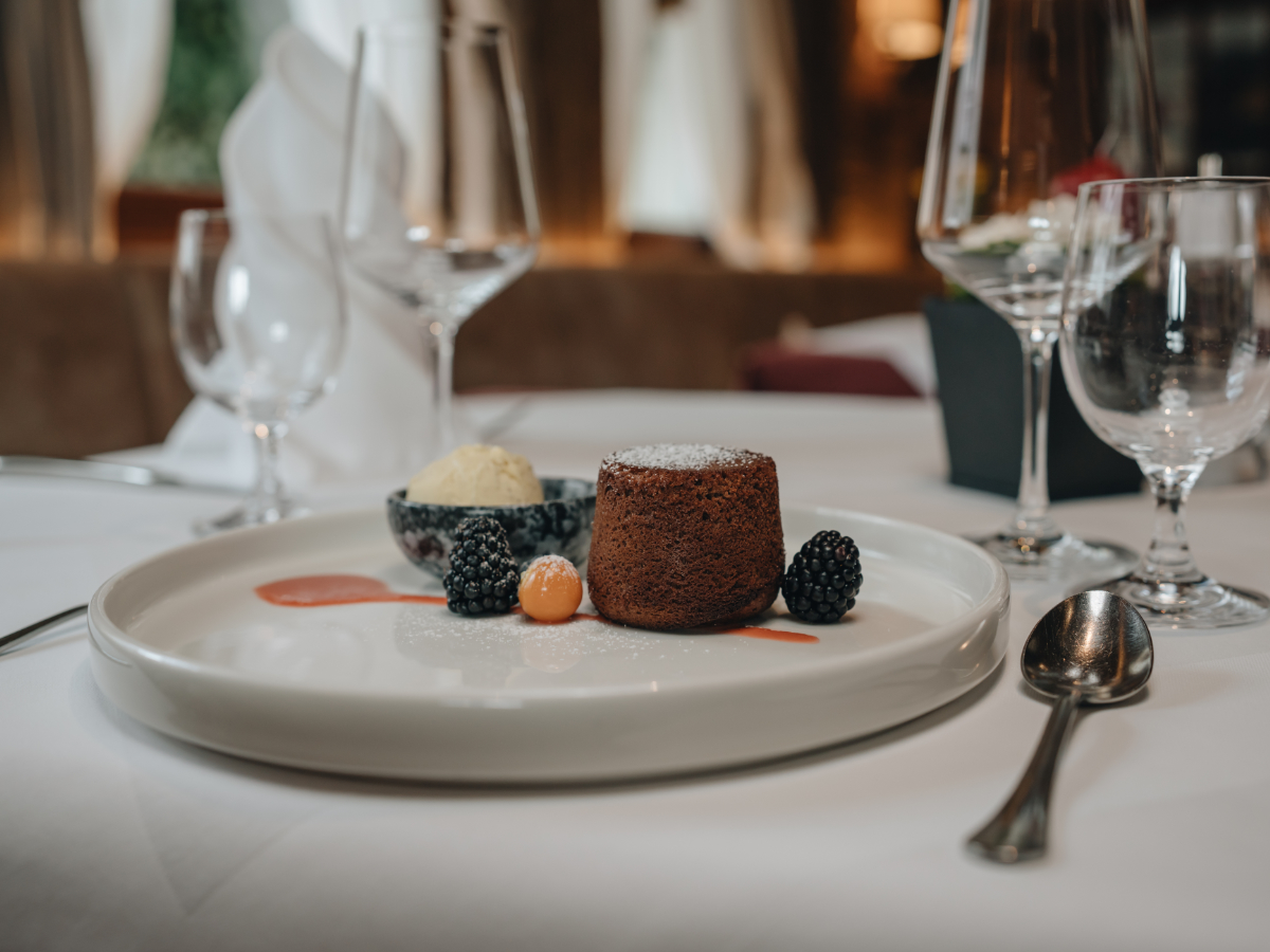 Schokoladenfondant mit Beeren und Eiscreme auf einem weißen Teller, gedeckt auf einem Restauranttisch.