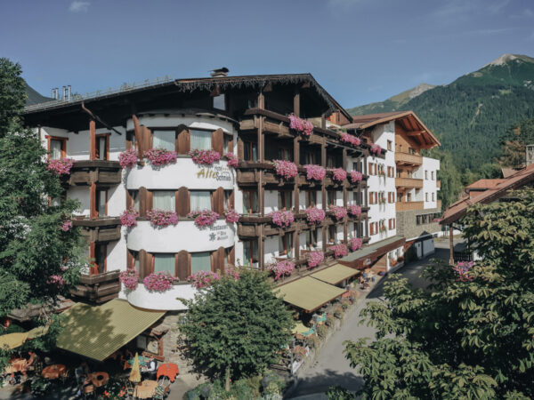 Hotel alpino con balconi fioriti, posti a sedere all'aperto e sfondo montano.