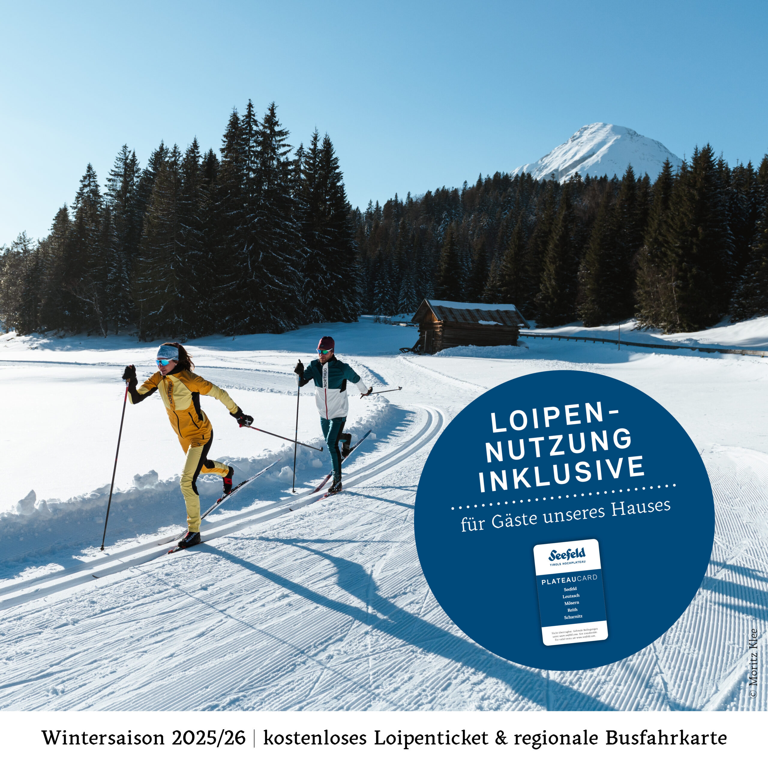 Zwei Personen beim Skilanglauf auf einer verschneiten Loipe mit Bergen und Bäumen im Hintergrund.