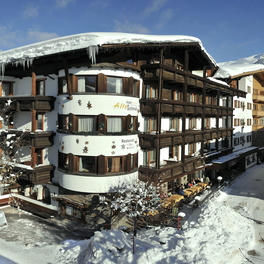 Snow-covered 4 star hotel Seefeld with wooden balconies and outdoor seating on a sunny winter day.