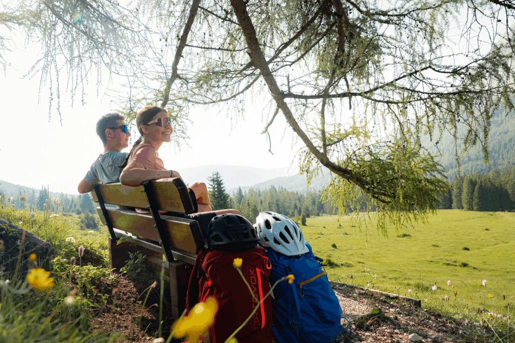 Zwei Personen sitzen auf einer Bank im Freien mit Seefeld-Golfhelmen und blicken auf eine malerische Wiese.