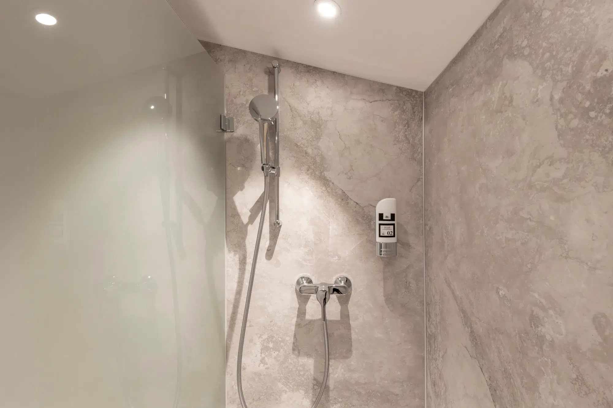 Moderne Dusche mit Steinmustern an den Wänden, Handbrause und eingebautem Seifenspender.