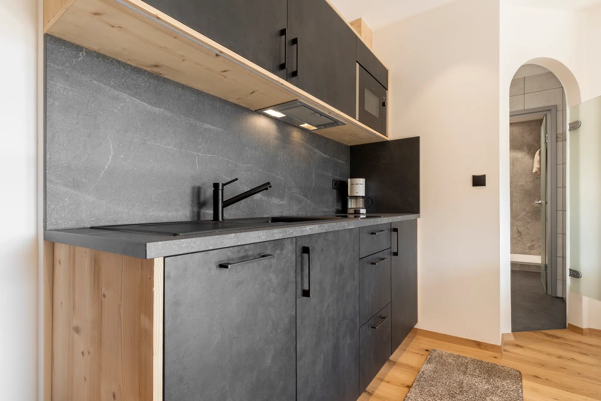 Moderne Küche mit schwarzen Schränken, grauer Arbeitsplatte, Spüle und Kaffeemaschine.